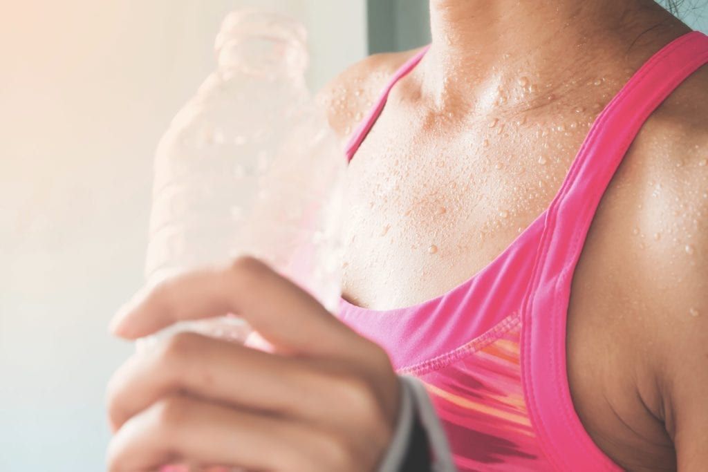 closeup of a woman sweating and drinking water after a workout