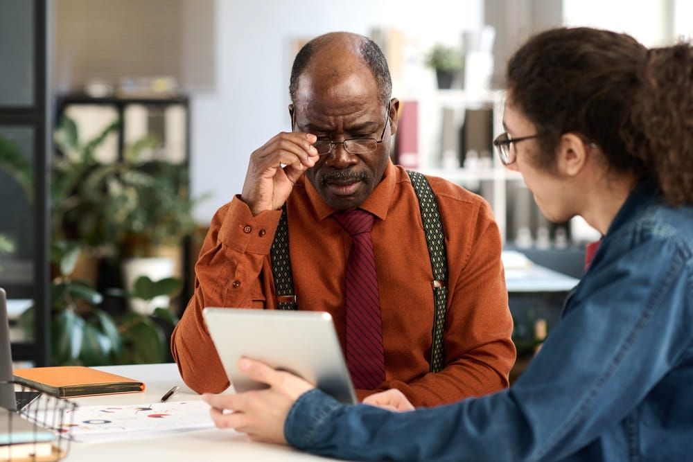Portrait of African American senior man adjusting glasses while looking at tablet screen in business meeting