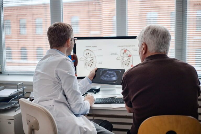 Middle aged Caucasian male doctor showing ultrasound image to senior man while discussing kidney health in medical office